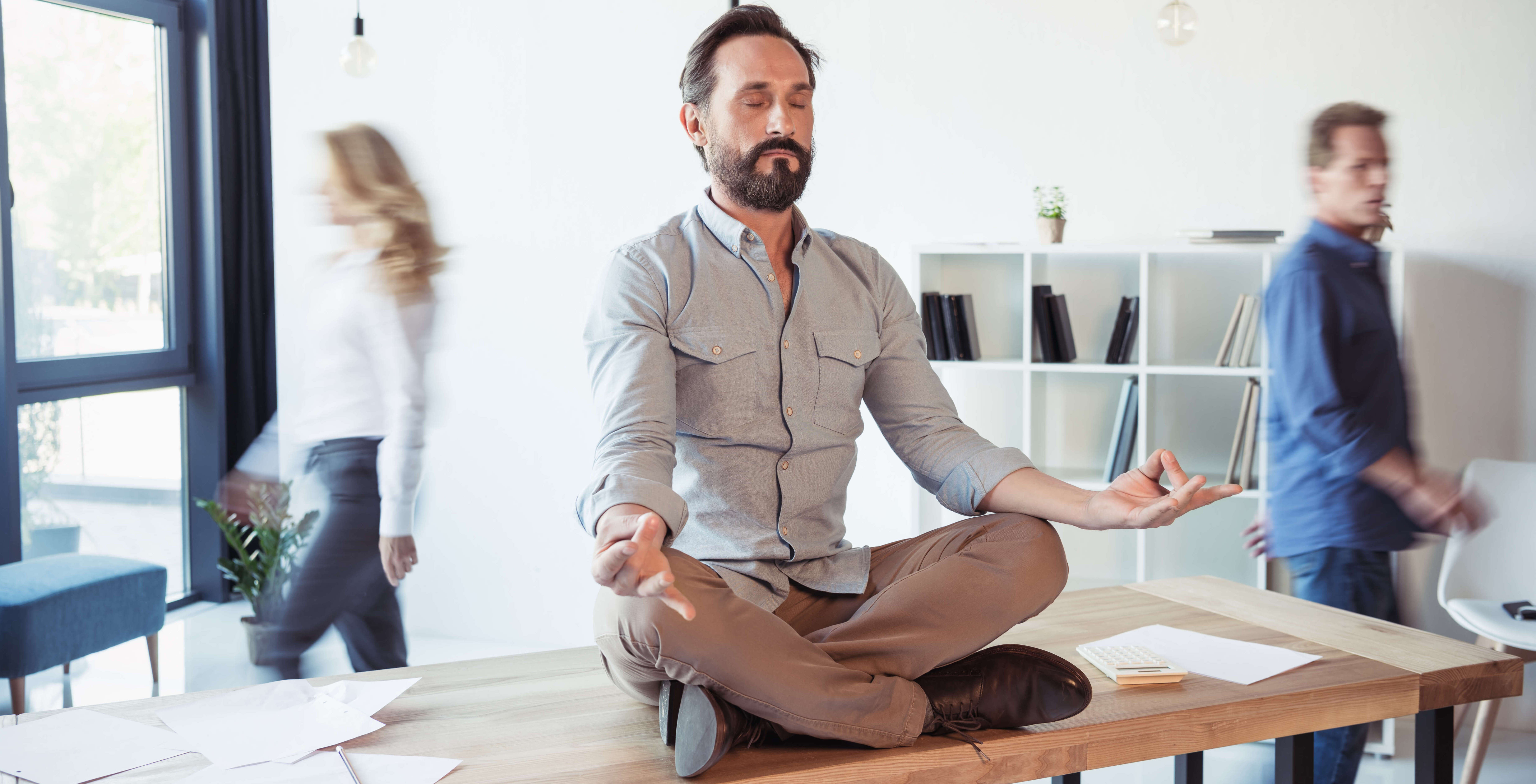 Businessman meditating in lotus position while colleagues move around in coworking office